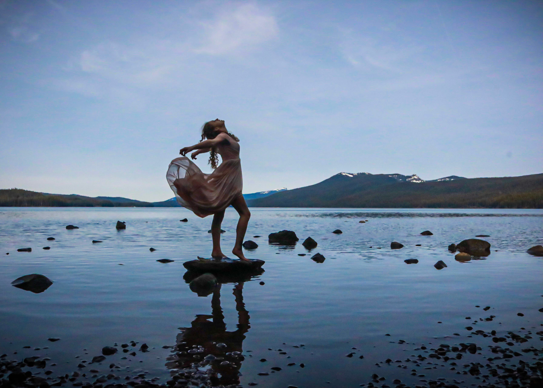 Woman dancing on lake rocks at sunset